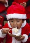 Una niña vestida de Santa Claus come un pastel después de su primer festival navideño.