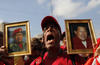 A supporter of Venezuela's late President Hugo Chavez holds images of him while the coffin containing his body passes in the street, from the hospital where he died on Tuesday to a military academy where it will remain until his funeral in Caracas, Venezuela, Wednesday, March 6, 2013. Seven days of mourning were declared, all schools were suspended for the week and friendly heads of state were expected for an elaborate funeral Friday. (AP Photo/Rodrigo Abd)