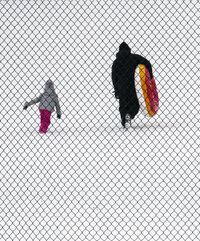 Seen through a basketball court's chain link enclosure, tubers head back up a hill for another run on the fresh snow at Raleigh Court Park on Monday Jan. 17, 2022 in Roanoke, Va. (AP Photo/Don Petersen)
