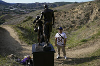 Oscar Romero stands near a statue in memory of former Los Angeles Lakers NBA basketball player Kobe Bryant and his daughter, Gianna, on Wednesday, Jan. 26, 2022, in Calabasas, Calif. The statue was carried by the artist, Dan Medina, on a trail near where Bryant, his daughter, and seven other people died in a helicopter crash two years ago Wednesday. (AP Photo/Ashley Landis)