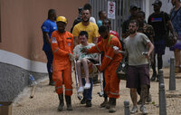 Rescue workers help a resident to evacuate an area under new landslide risk in Petropolis, Brazil, Thursday, Feb. 17, 2022.  Deadly floods and mudslides swept away homes and cars, but even as families prepared to bury their dead, it was unclear how many bodies remained trapped in the mud. (AP Photo/Silvia Izquierdo)