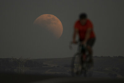 A lunar eclipse is seen behind a cyclist during the first blood moon of the year, in Irwindale, Calif. May 15, 2022. (AP Photo/Ringo H.W. Chiu)

