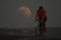A lunar eclipse is seen behind a cyclist during the first blood moon of the year, in Irwindale, Calif. May 15, 2022. (AP Photo/Ringo H.W. Chiu)