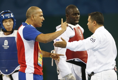 El taekwondista cubano Angel Valodia Matos (c) y su entrenador (iz) discuten con el árbitro,el sueco Chakir Chelbat, momentos antes de que Valodia le diese una patada tras ser descalificado en la pelea por el bronce, categoría de 80 kilos, con el kazajo Arman Chilmanov, que fue declarado vencedor. EFE