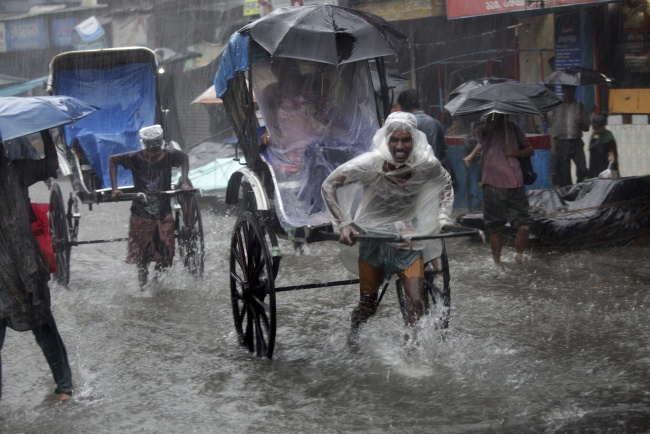 Conductores de 'ricksaws' corren bajo la lluvia llevando a pasajeros por las calles inundadas de Calcuta. EFE