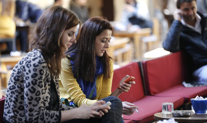 Dispositivos. En la fotografía aparecen dos mujeres que escriben en sus teléfonos móviles en una cafetería. 