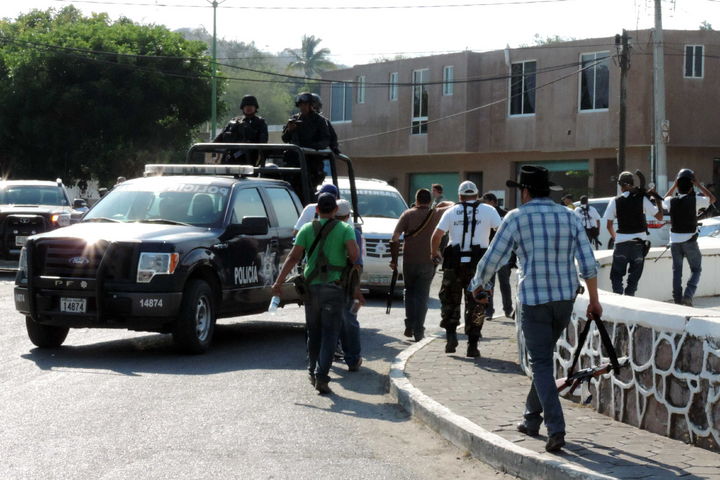 Recorrido. Miembros de autodefensas recorriendo Arteaga, Michoacán, mientras policías federales patrullan las avenidas.
