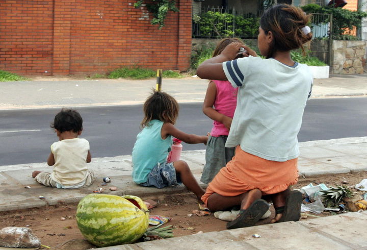 Pobreza. Una mujer peina a sus hijas mientras comparten una sandía en plena calle.