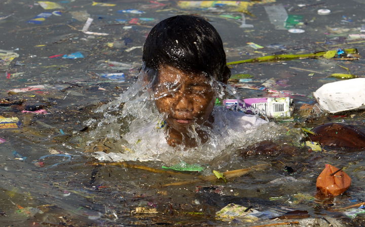 Medio ambiente. Un joven en Manila nada en un estanque lleno de basura, como parte de lo que se vive actualmente en el mundo. (AP)