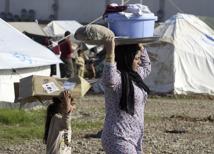 Ataque. Una mujer  yazidi con su hija llevan comida y ropa en el campo de refugiados, tras un ataque del Estado Islámico. 