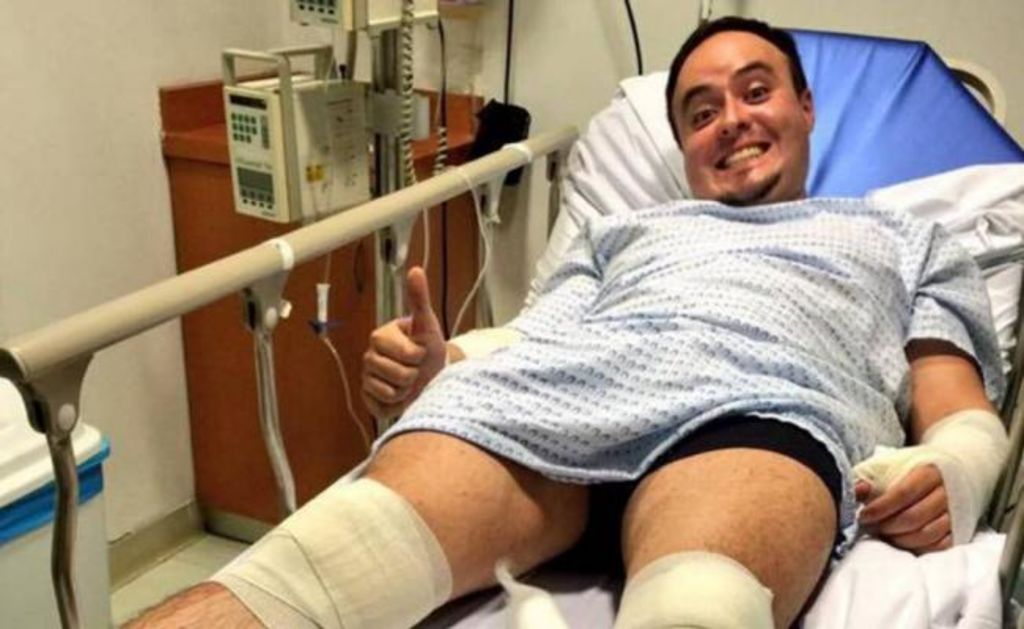 En una fotografía se observa postrado sobre una cama de hospital con el brazo enyesado y vendas en las piernas. (FACEBOOK)