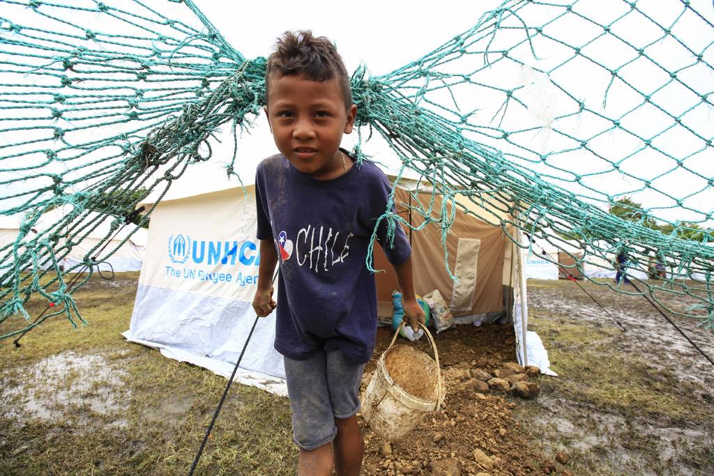 Escenario. Un niño en un campo de refugiados sostiene una cubeta para ir por agua. 