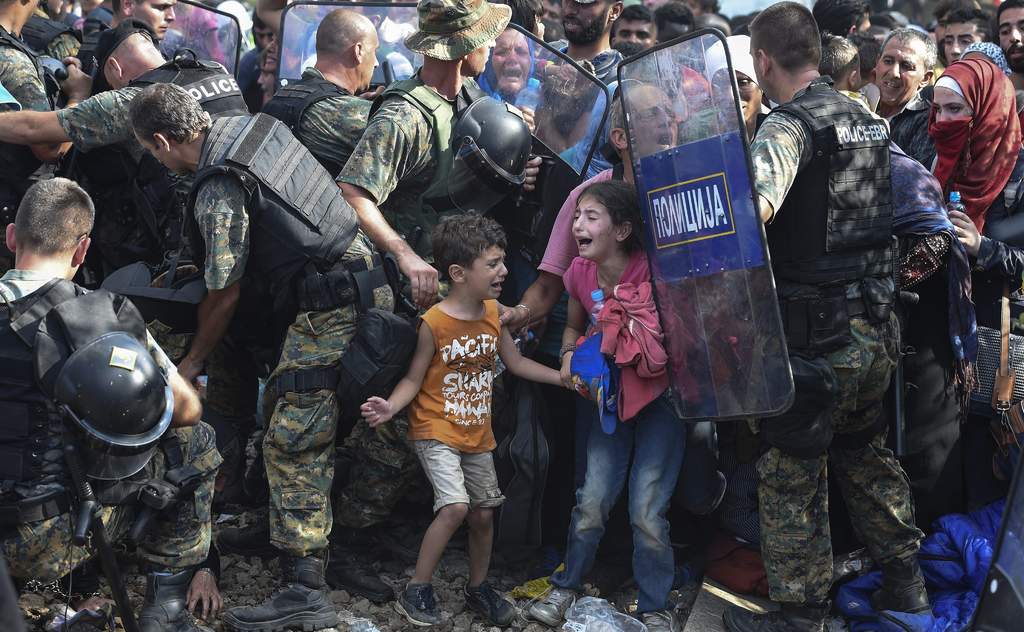 Barrera. Dos niños migrantes lloran mientras otros refugiados intentan romper el cordón policial  para cruzar a Macedonia.