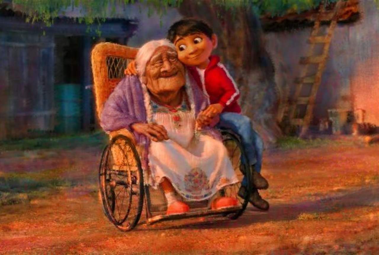 La imagen muestra a “Héctor” un pequeño niño de cabello negro abrazando a su abuela sentada en una silla de ruedas, quien porta un traje típico regional blanco bordado en brillantes colores. (TWITTER) 
