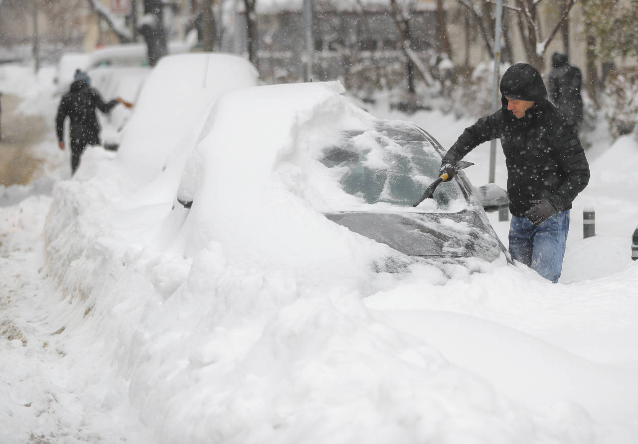 Cubiertos. Una persona quita la nieve a su auto, la cual se acumuló por la nevada en Bucarest.