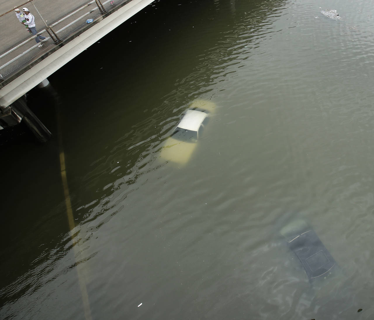 Superior. Personas observan los autos que encontraron debajo del agua en una autopista. (AP)