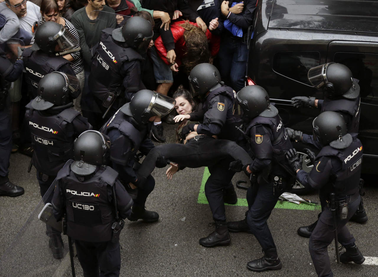 Agentes antidisturbios de la Policía Nacional que han formado un cordón de seguridad trasladan a una joven frente al colegio Ramón Llull de Barcelona. (EFE)