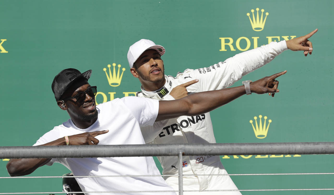 Lewis Hamilton y Usain Bolt hacen la pose clásica del jamaiquino, en la premiación del GP de EU. (AP)