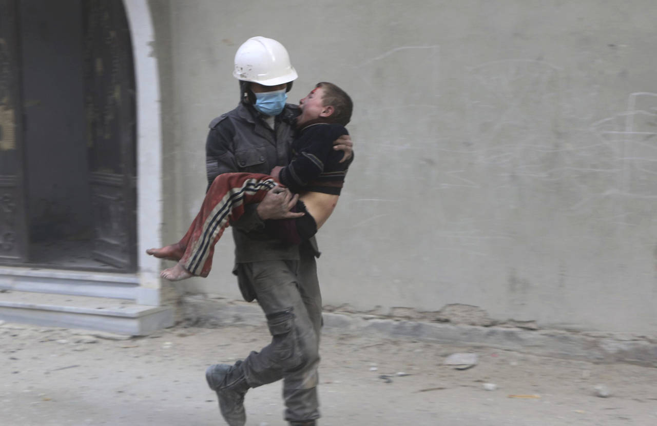 Salvarlo. Un miembro de los Cascos Blancos carga a un niño luego de uno de los bombardeos que golpeó nuevamente a Guta Oriental. (AP y EFE)
