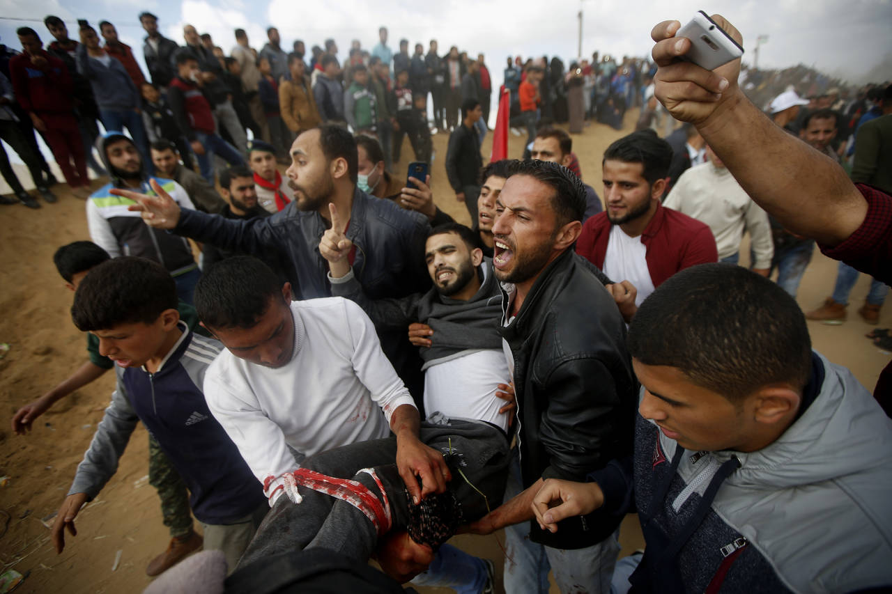 Conflicto abierto. Manifestantes palestinos auxilian a un joven herido durante el choque con fuerzas armadas israelíes en Gaza.