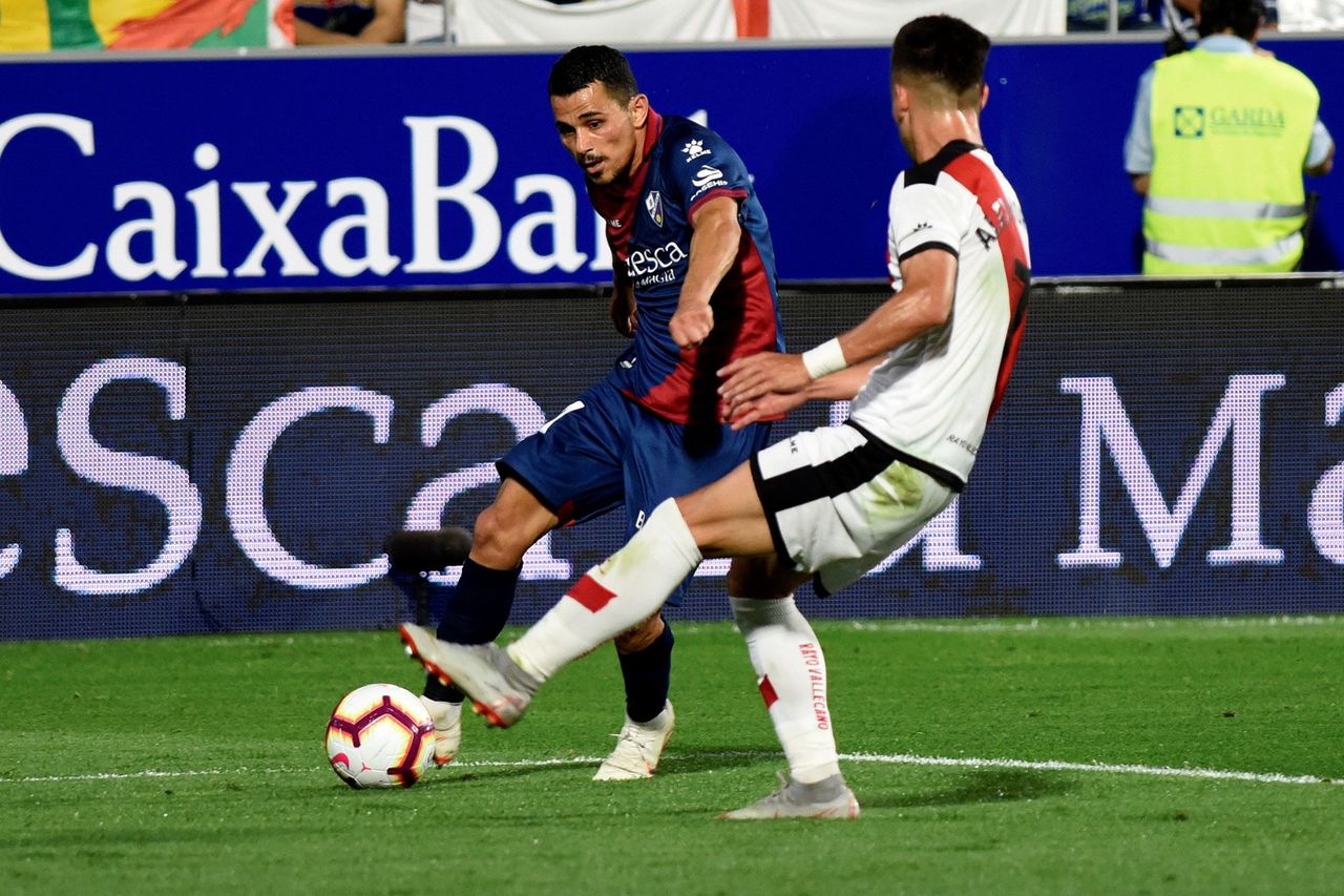 El centrocampista francés del Huesca, Serdar Gurler (i), golpea el balón ante el jugador del Rayo, Alex Moreno.