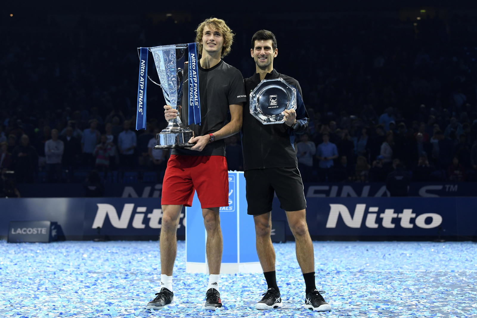 Alexander Zverev y Novak Djokovic sostienen sus respectivos trofeos.