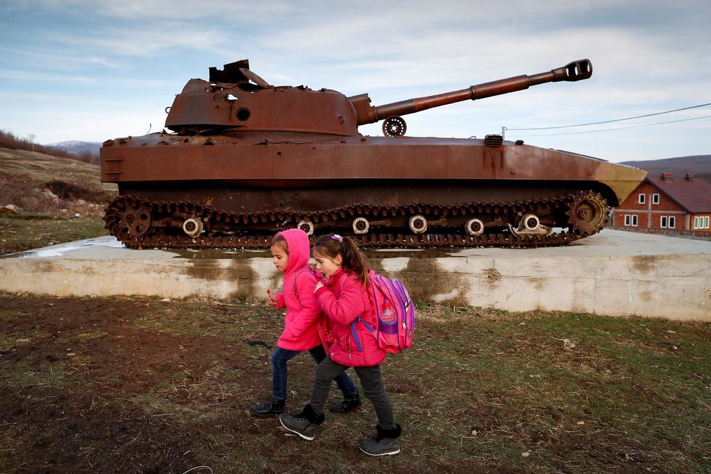 Unas niñas regresan de la escuela y al lado se observa un tanque.