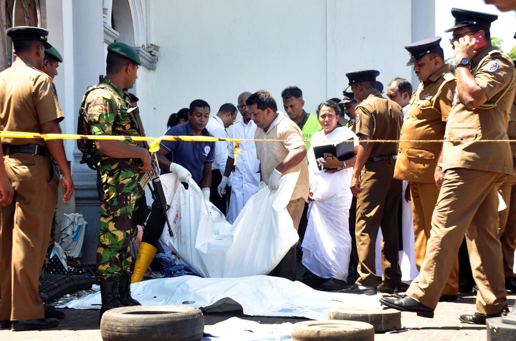 La policía y los equipos de rescate inspeccionan los restos de las víctimas después de una explosión en la iglesia en Kochchikade.  (EFE y AP)