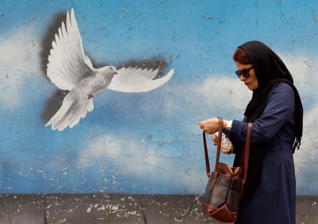 Mujer pasea junto a obra mural, en la víspera del primer año en el que EUA decidió abandonar el acuerdo nuclear multilateral de 2015. (AGENCIAS)