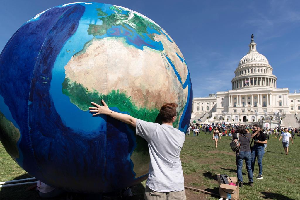 En Washington, un joven abraza un enorme globo terráqueo frente al Capitolio, donde la gente que participó en las protestas se muestra dispersa en los jardines. Una de tantas manifestaciones que se registraron ayer para exigir contundencia ante la crisis climática.