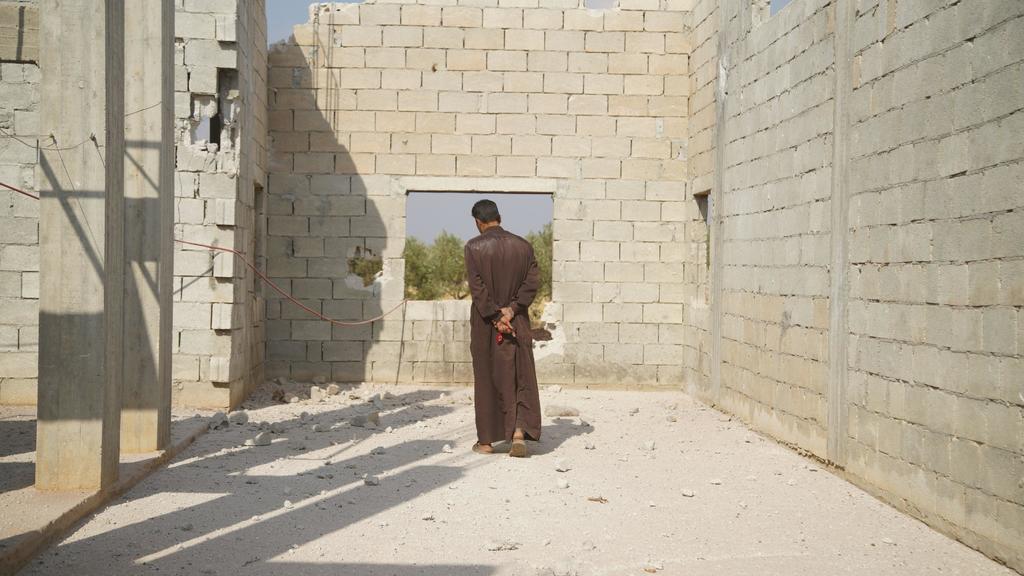 Un hombre permanece en pie frente a una ventana de la edificación cercana a la zona en la que uno de los helicópteros estadounidenses abrió fuego para asesinar al líder del Estado Islámico. (EFE)