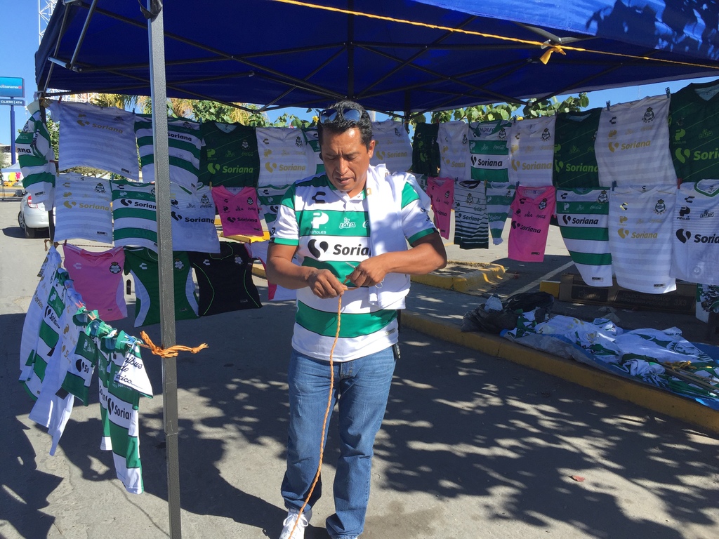Don Enrique Hernández se instaló debajo de un toldo en un estacionamiento de un centro comercial para ofrecer playeras y banderas del Santos Laguna. (GUADALUPE MIRANDA)