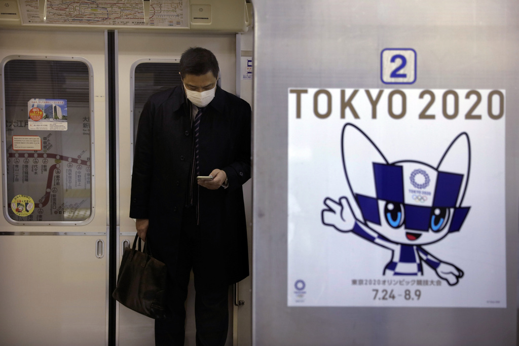 Un cartel de los Juegos Olímpicos de Tokio 2020 es visto junto a la puerta un tren del metro mientras un viajero con una máscara mira su celular, ayer, en Tokio. (AP)