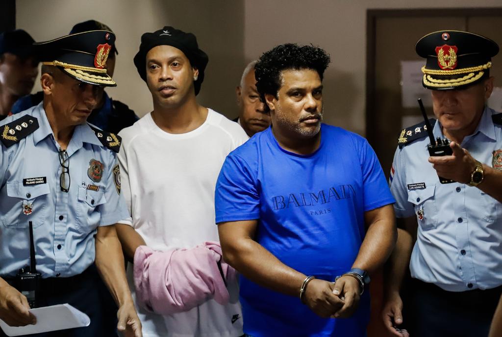 El jugador de 39 años y su hermano Roberto Assis fueron arrestados la noche del viernes en un hotel de la capital de Paraguay. Ambos aparecieron el sábado esposados y Ronaldinho trataba de ocultar las esposas bajo un trozo de tela lila.
(EFE)