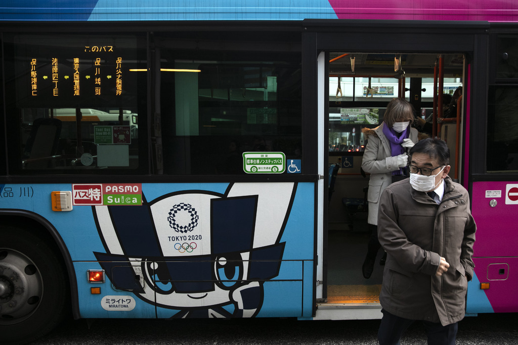 Pasajeros luciendo cubrebocas se bajan de un autobús con publicidad de los Juegos Olímpicos de Tokio 2020. (AP)
