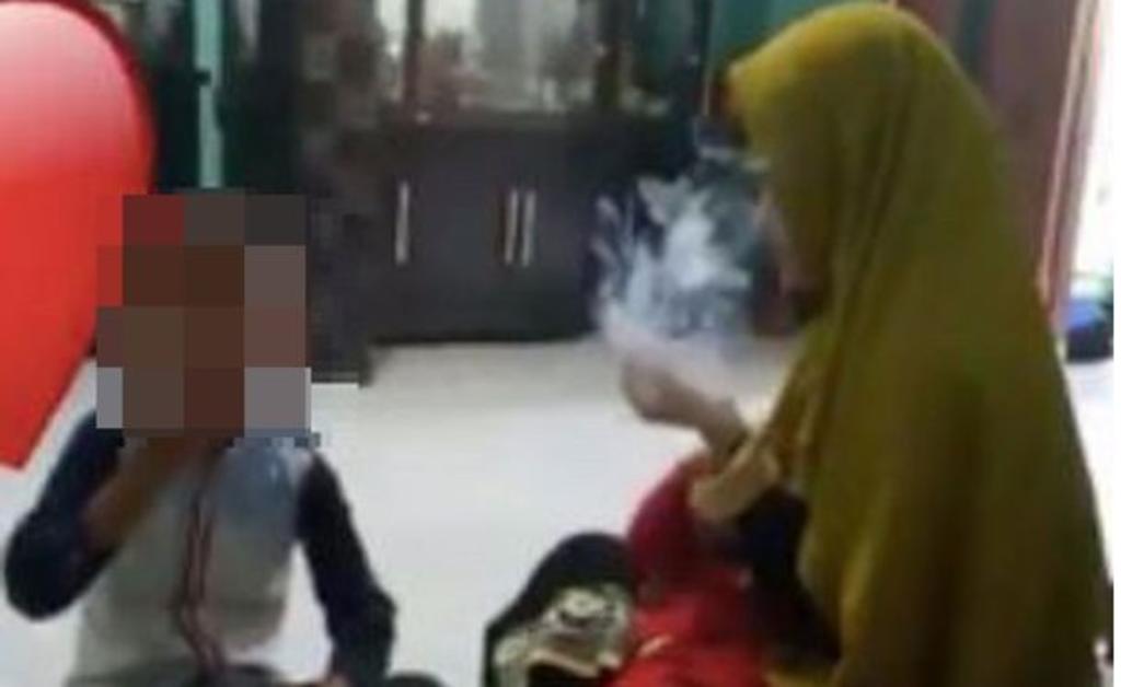 En el video se aprecia a tres menores compartir cigarrillos con los adultos mientras permanecen sentados en el suelo (MATERIAL: MIRROR)  
