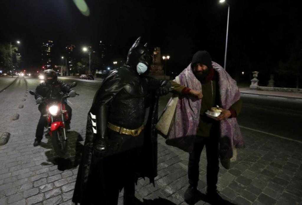 Complementando su disfraz con un cubrebocas, el hombre vestido de 'Batman' reparte comida entre los más necesitados por las calles de Santiago de Chile (CAPTURA) 