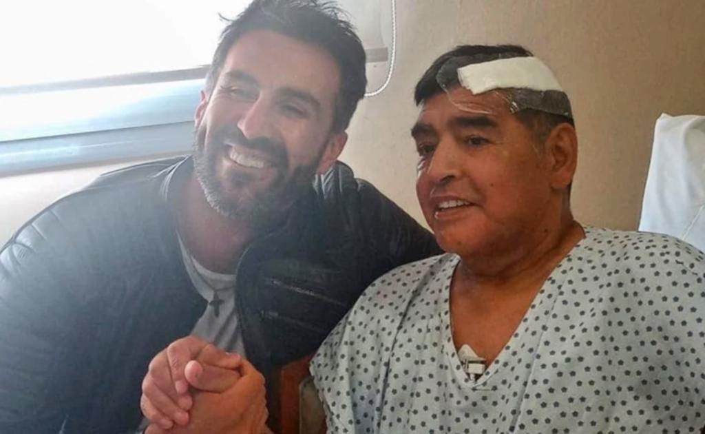 En la imagen se ve a un sonriente Diego Armando Maradona vestido con un bata clínica y un vendaje en la parte lateral del cráneo, a lado de Leopoldo Luque.

(EFE)
