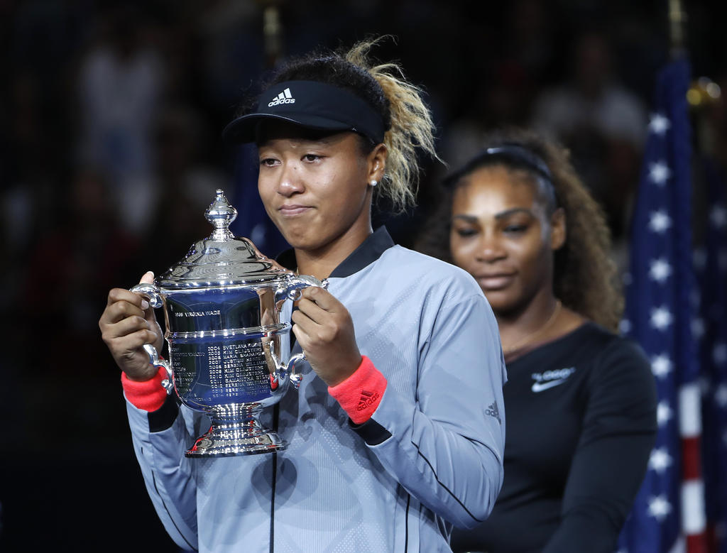 Naomi Osaka posa con el trofeo que ganó tras derrotar a Serena Willims (detrás suyo) en la final del US Open el 8 de septiembre del 2018. (AP Photo/Adam Hunger, File)