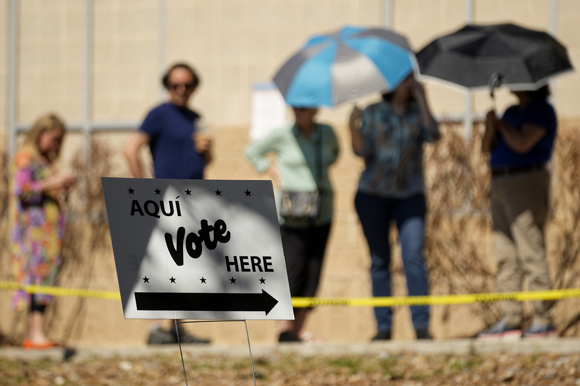 Votantes usan sombrillas para cubrirse del sol mientras esperan formados en un centro de votación, el martes 5 de marzo de 2024, en San Antonio. (AP Foto/Eric Gay)