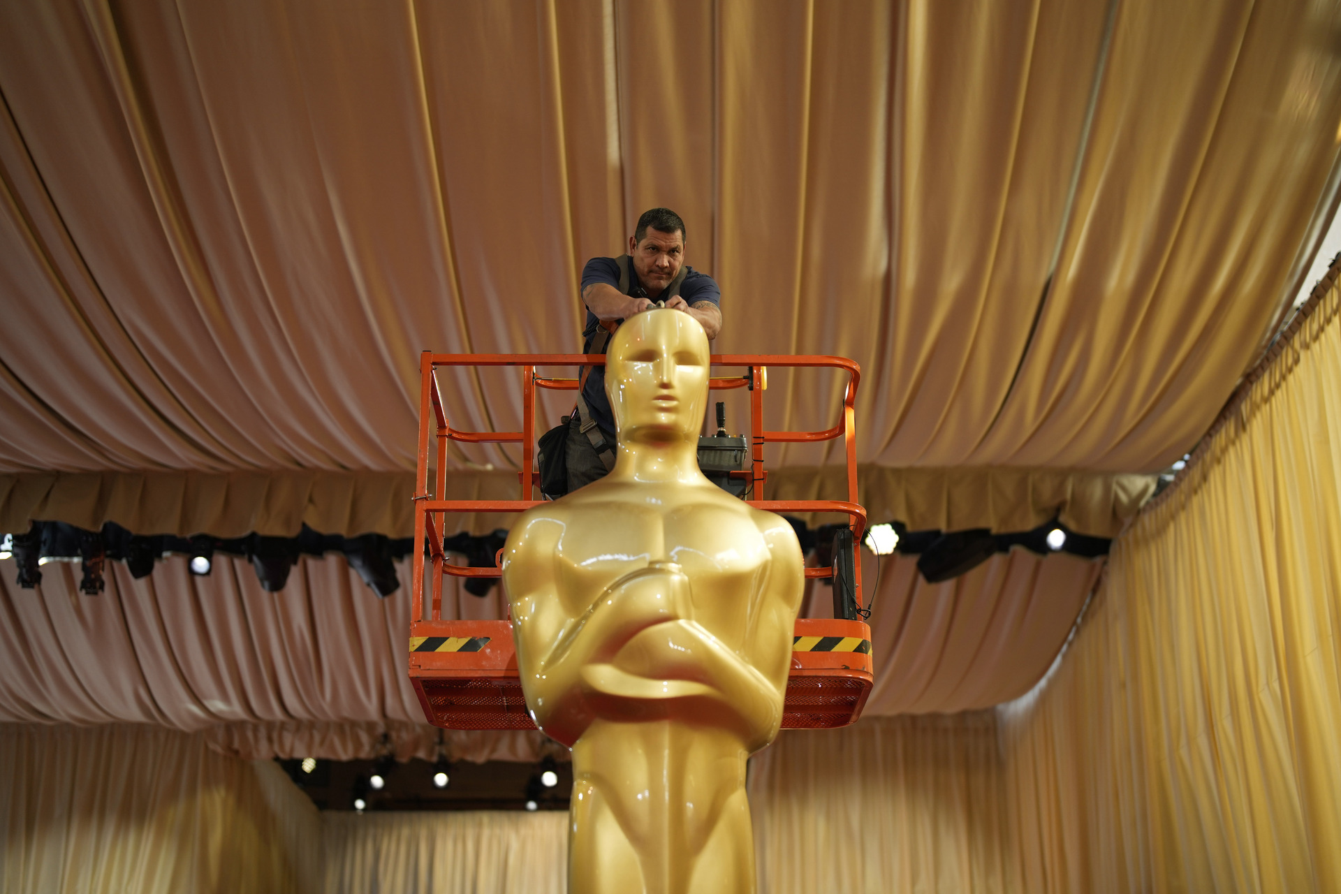 Un trabajador ayuda a colocar una estatua de los Oscar en la alfombra roja previo a la 96a entrega de los Premios de la Academia. (AP)